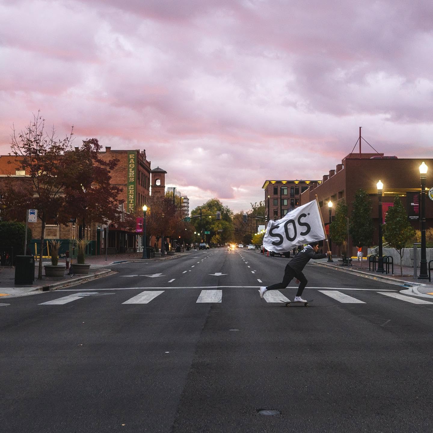 Skateboarder carrying a large SOS flag through downtown Boise